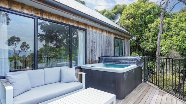 A modern outdoor deck with a hot tub, a white sofa, and a dining table. - Bushside Cottage - Akaroa Holiday Home (Akaroa)
