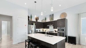 A modern kitchen with a large island, bar stools, stainless steel appliances, and pendant lighting. - Reunion Resort Villa: Private Pool, Full Amentiy Access (Reunion)