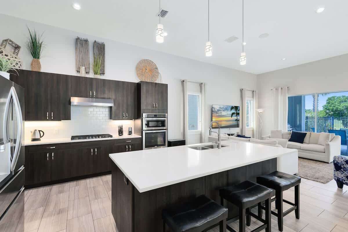 A modern kitchen with dark wood cabinets, a white island, stainless steel appliances, and a large window.