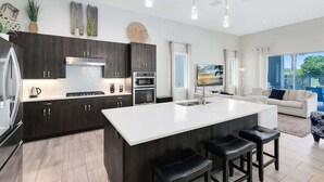 A modern kitchen with dark wood cabinets, a white island, stainless steel appliances, and a large window. - Reunion Resort Villa: Private Pool, Full Amentiy Access (Reunion)
