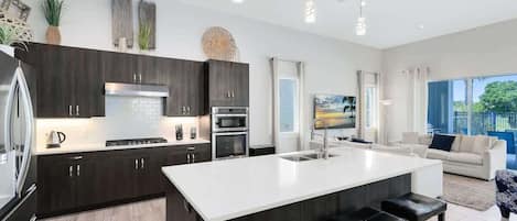 A modern kitchen with dark wood cabinets, a white island, stainless steel appliances, and a large window.