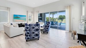 A spacious living room with a sofa, armchairs, and a dining table. There is a large window offering a view of the outdoors. - Reunion Resort Villa: Private Pool, Full Amentiy Access (Reunion)