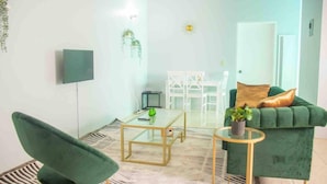 Un salon moderne avec un canapé vert, une table basse en verre, un fauteuil vert et une petite table sur laquelle est posée une plante.