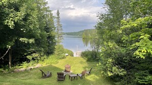 Ein grünes Freigelände mit einem Holztisch und Stühlen, umgeben von dichtem Grün und einem See im Hintergrund.
