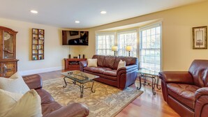 A spacious living room with a brown leather sofa, a glass coffee table, and a patterned rug.