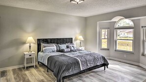 A bedroom with a large bed, two bedside tables with lamps, and a view of a yard through a window. - Palm Coast Home ~ 7 Mi to Flagler Beach! (Palm Coast)