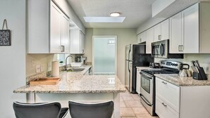 A modern kitchen with white cabinets, granite countertops, a black refrigerator, a microwave, and a stove. There are two black chairs at the kitchen island. - Palm Coast Home ~ 7 Mi to Flagler Beach! (Palm Coast)