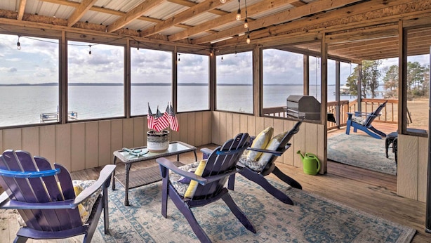 Een overdekt terras met Adirondack stoelen, een tafel met een Amerikaanse vlag en uitzicht op het water.
