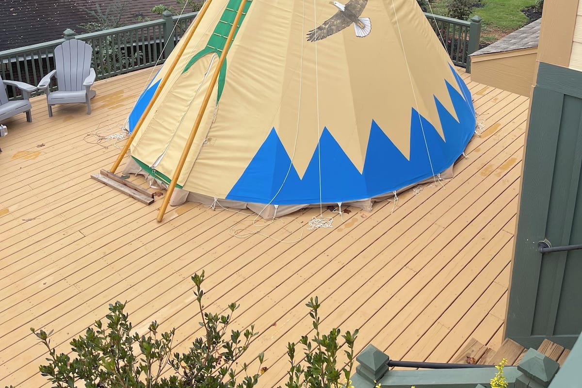 A large, colorful tent on a wooden deck with a view of a residential area and trees in the background.