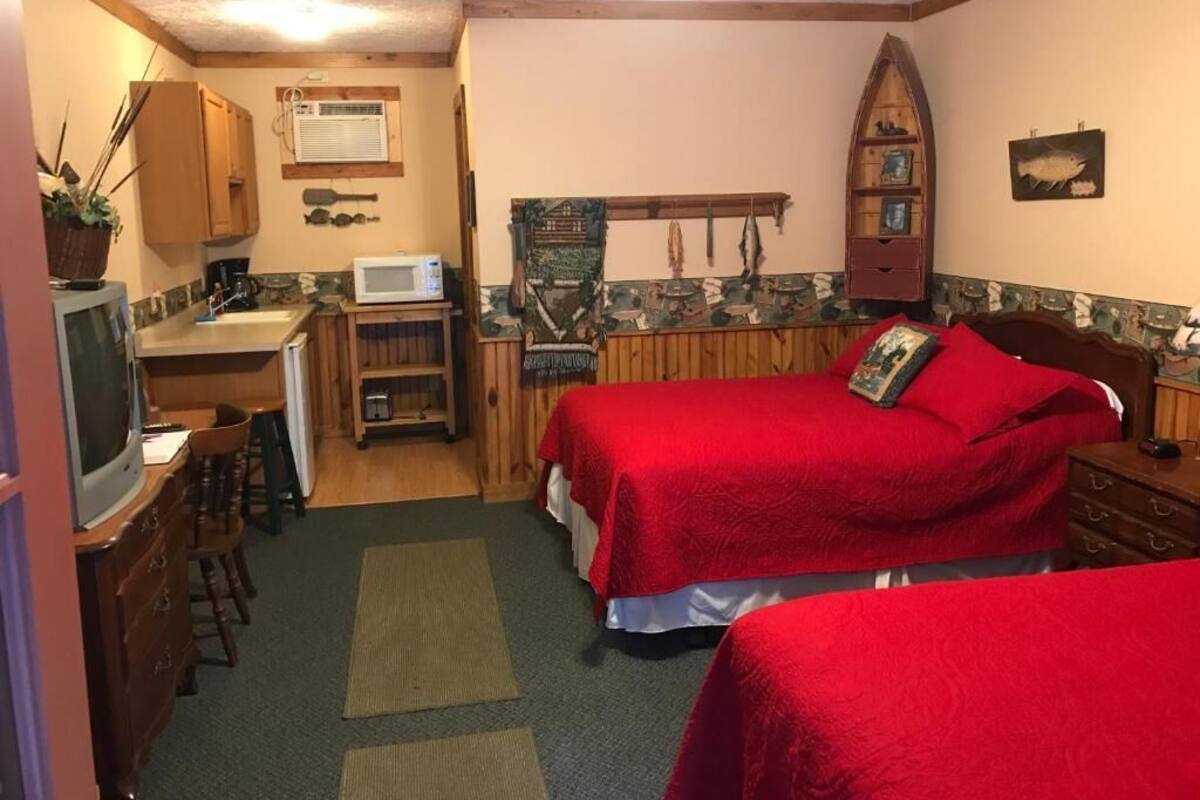 A compact room with two beds, a kitchenette, a television, and a small dining area.