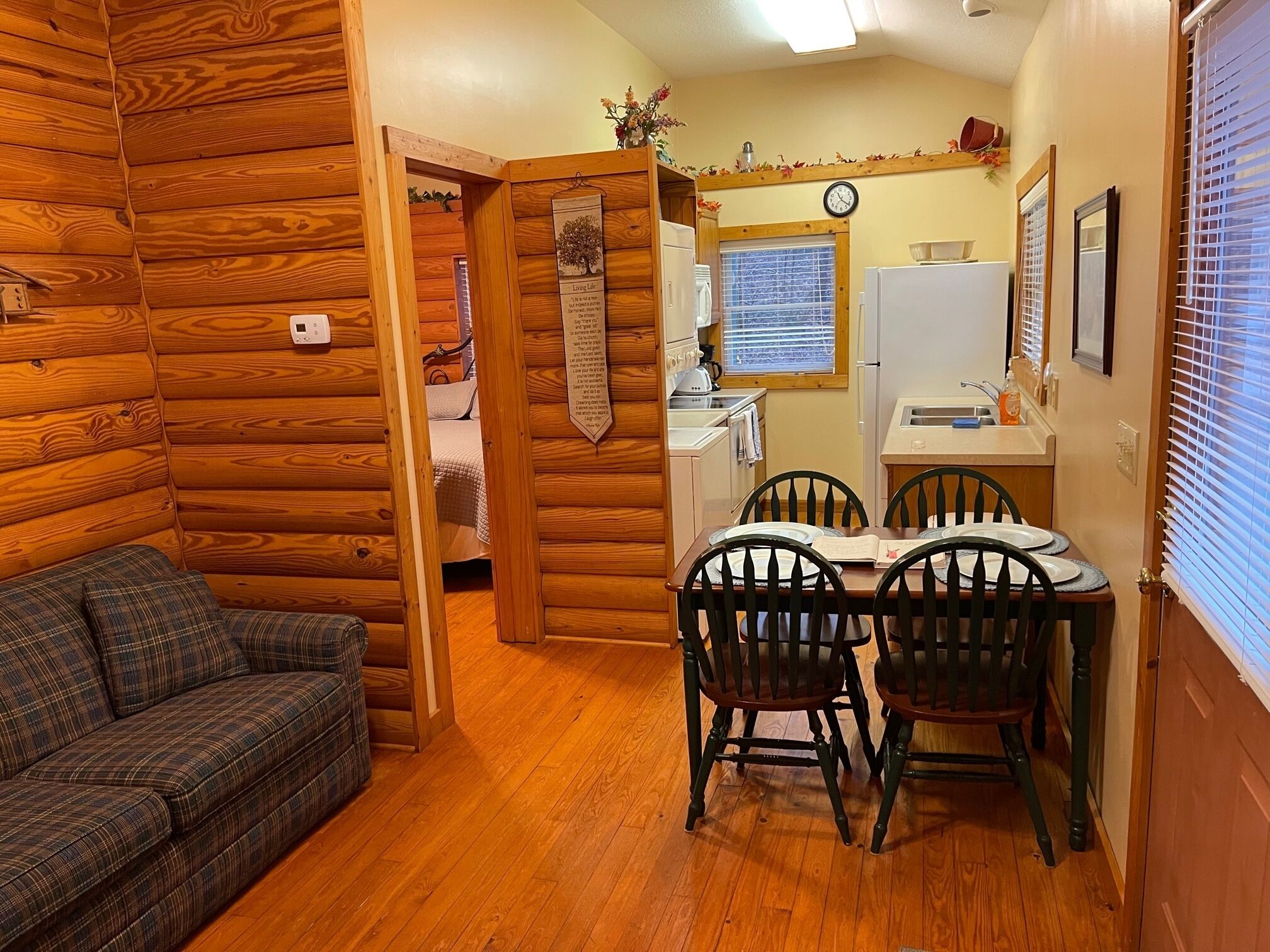 A cozy cabin interior with a wooden log wall, a dining area with a table and chairs, a kitchen with a refrigerator and sink, and a living area with a couch.