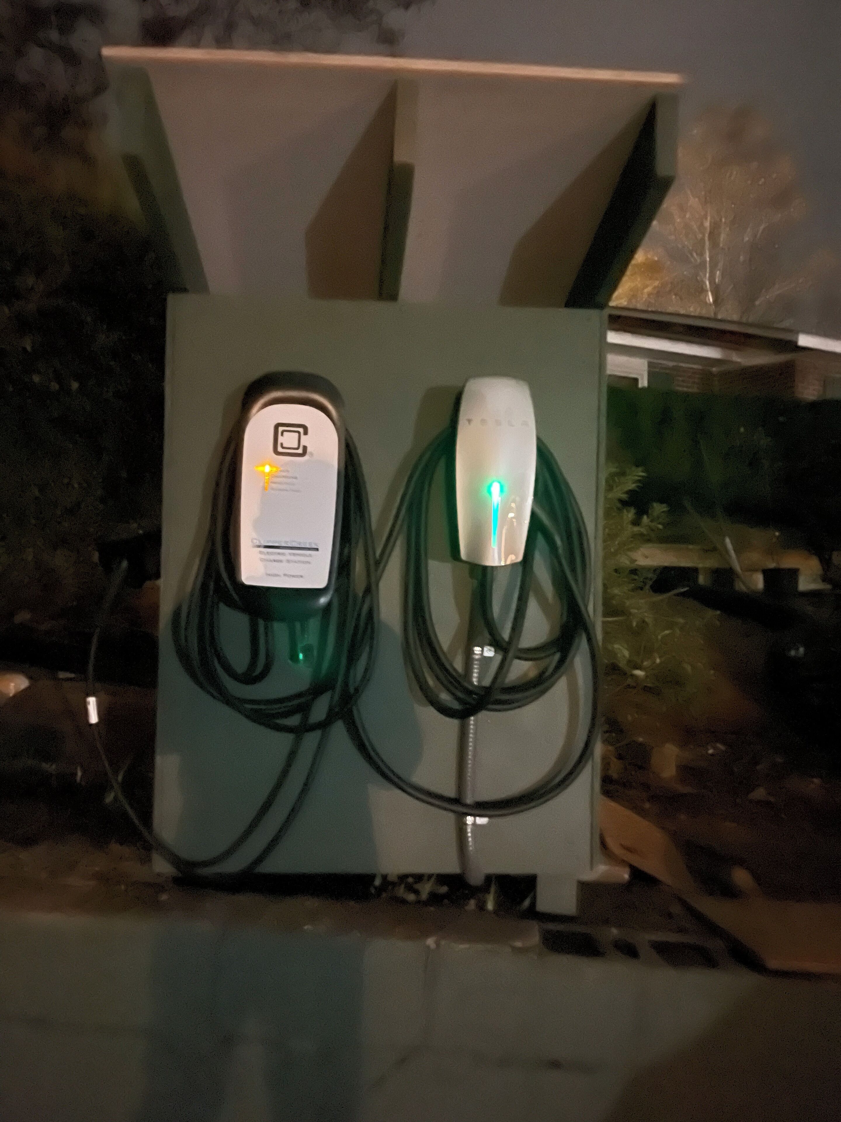 Una estación de carga con el logotipo de Tesla, un cable e indicador luminoso verde.