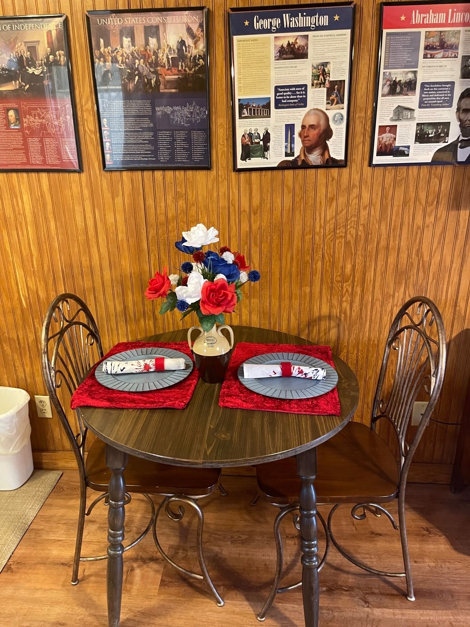 Una mesa de comedor con dos sillas, un jarrón de flores y posavasos.