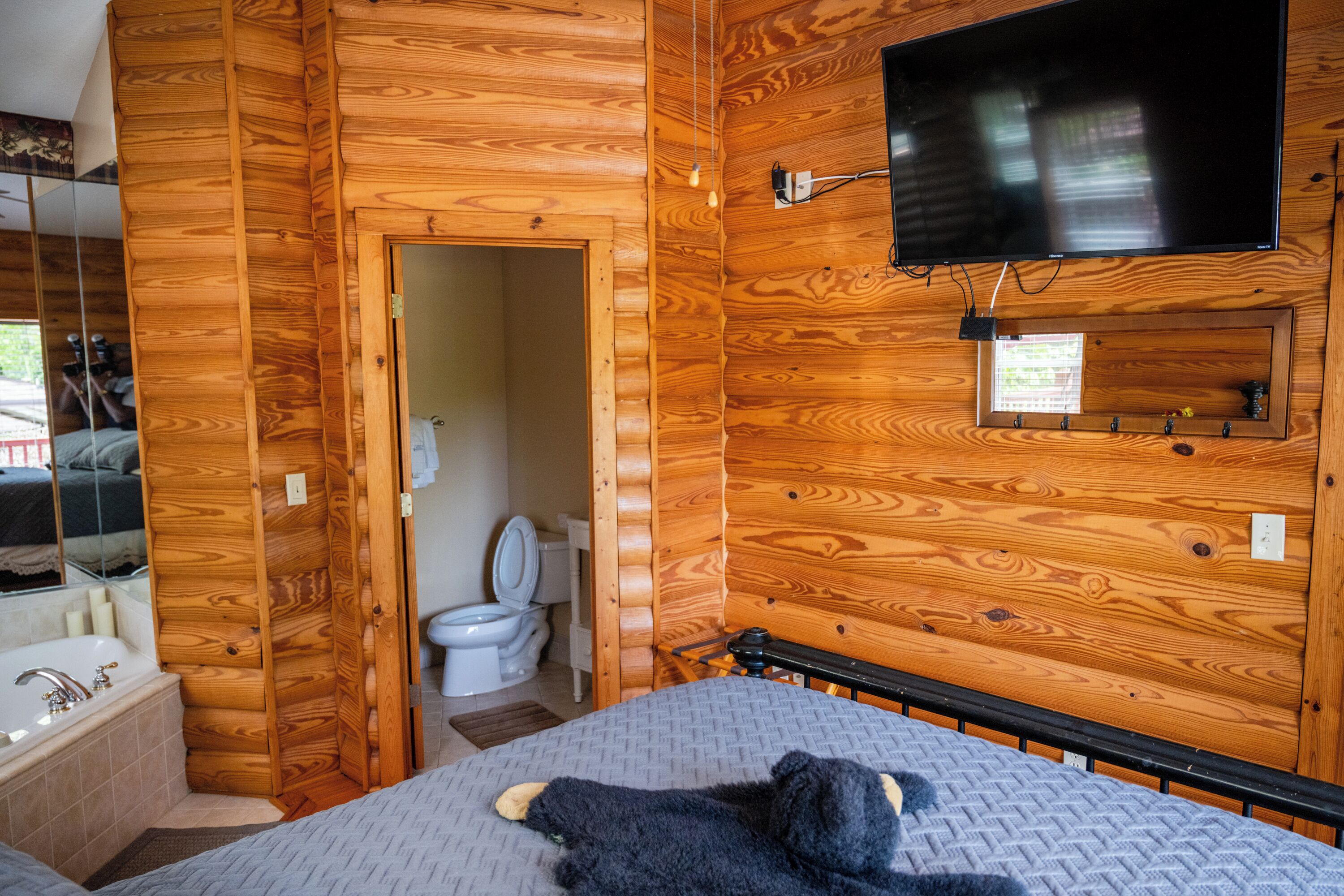 L’intérieur d’une cabane en bois comprend un lit, un téléviseur fixé au mur, une porte en bois et une salle de bain avec des toilettes et un lavabo.