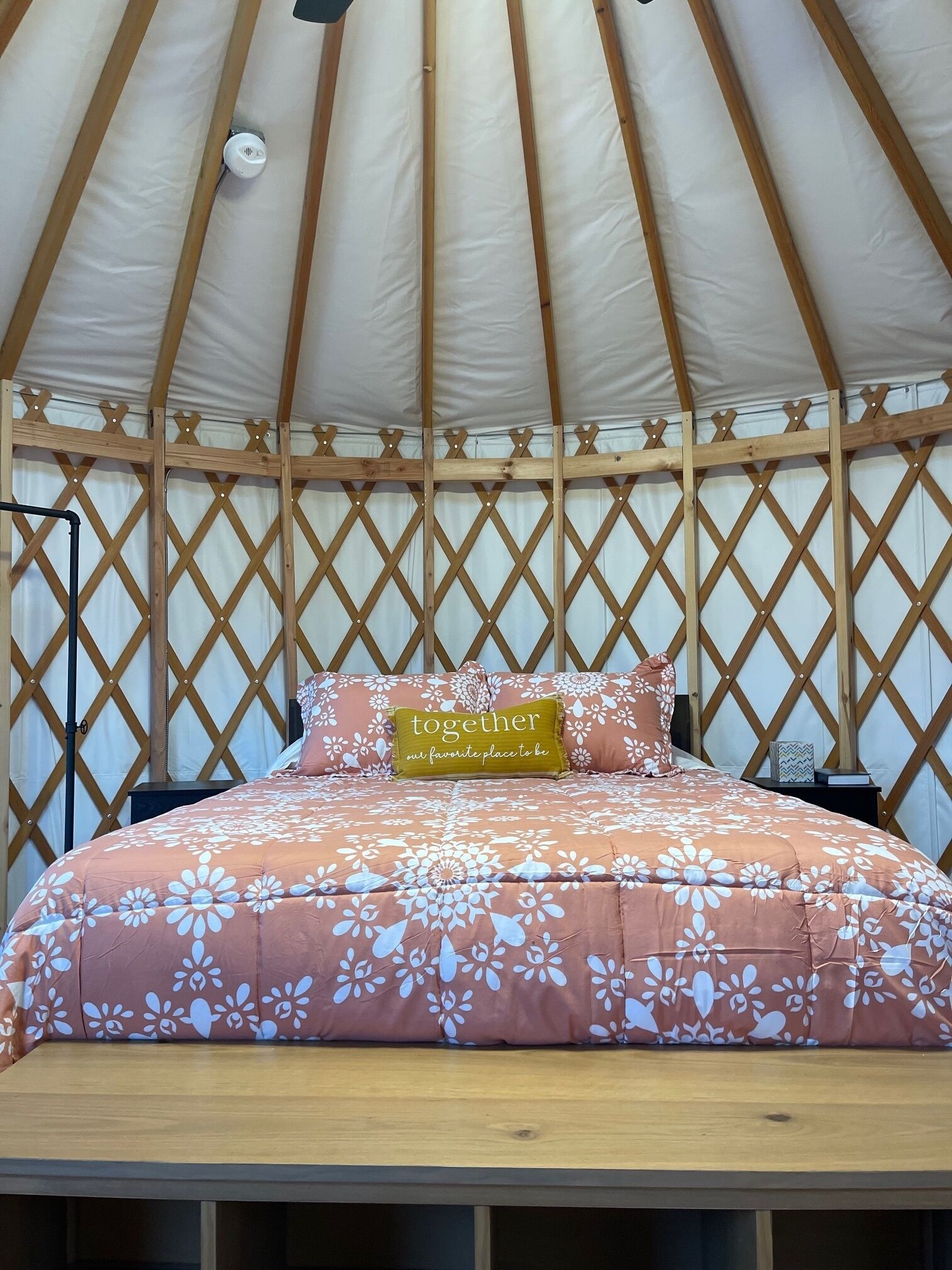 Un lit avec une couvre-lit à motifs floraux, un oreiller orné d’un texte et une tête de lit en bois, le tout installé dans une structure ressemblant à une tente.