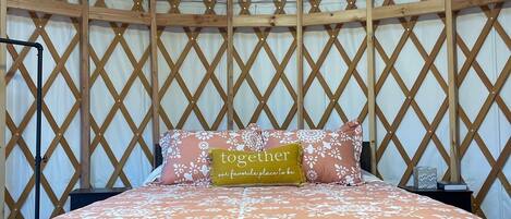 Un lit avec une couvre-lit à motifs floraux, un oreiller orné d’un texte et une tête de lit en bois, le tout installé dans une structure ressemblant à une tente.