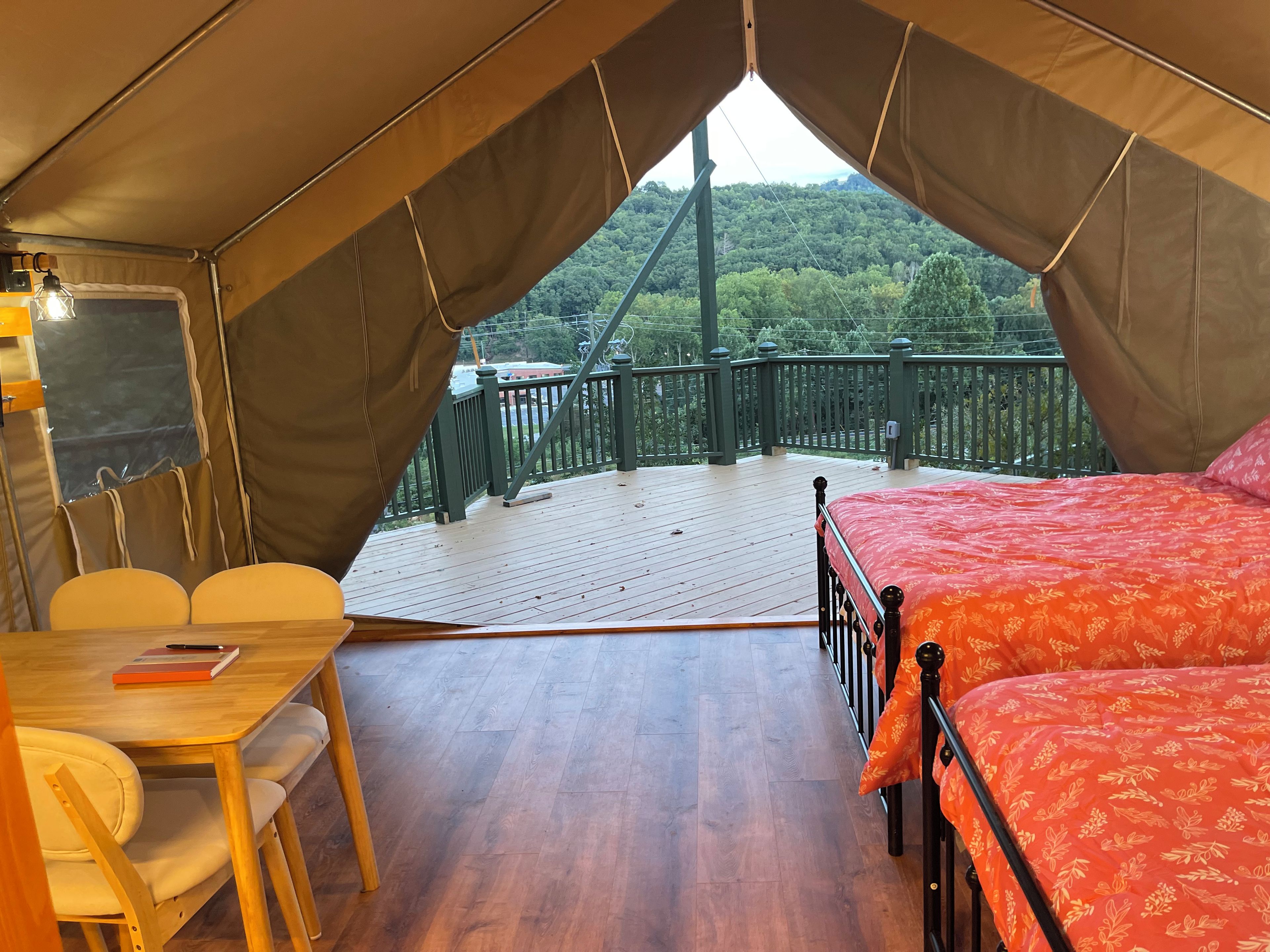 Una carpa con cama y mesa, vista de un área boscosa y una terraza de madera.