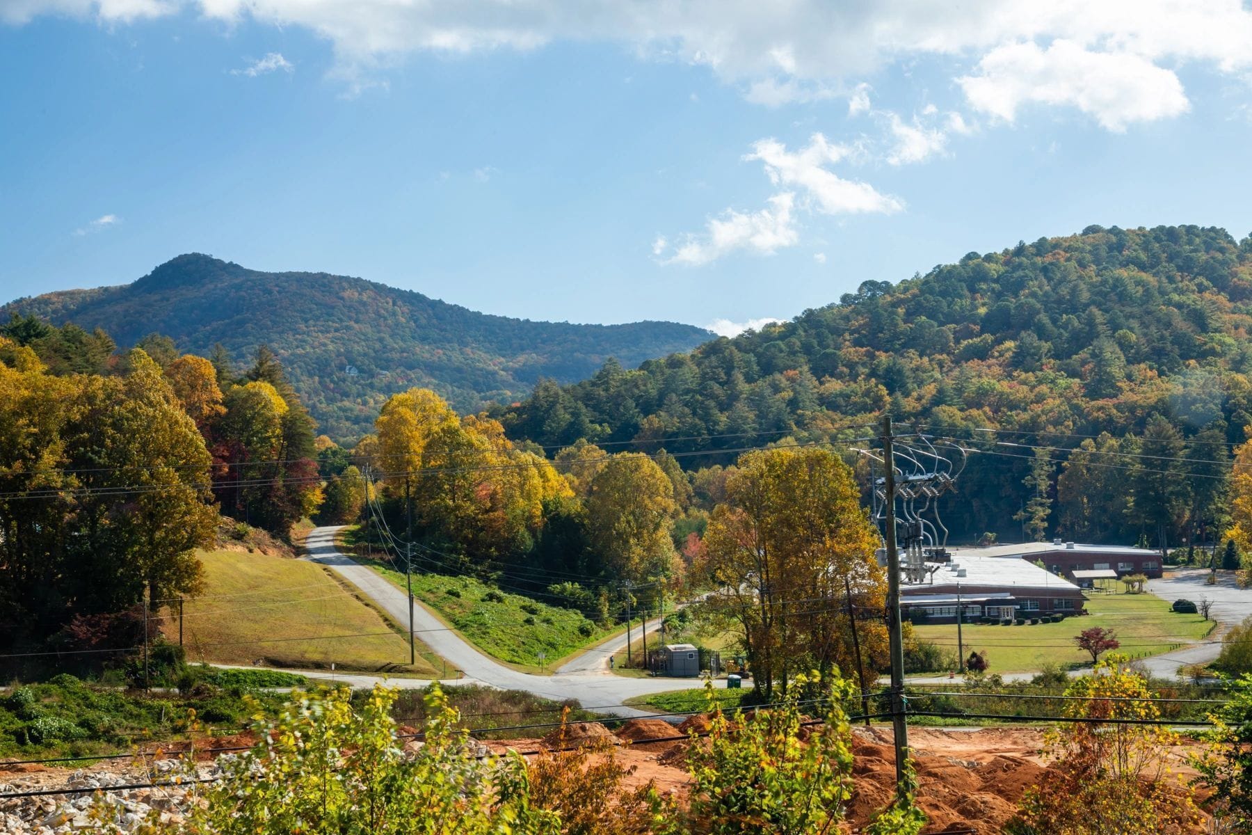 A rural landscape with a road, trees, and a building in the distance.