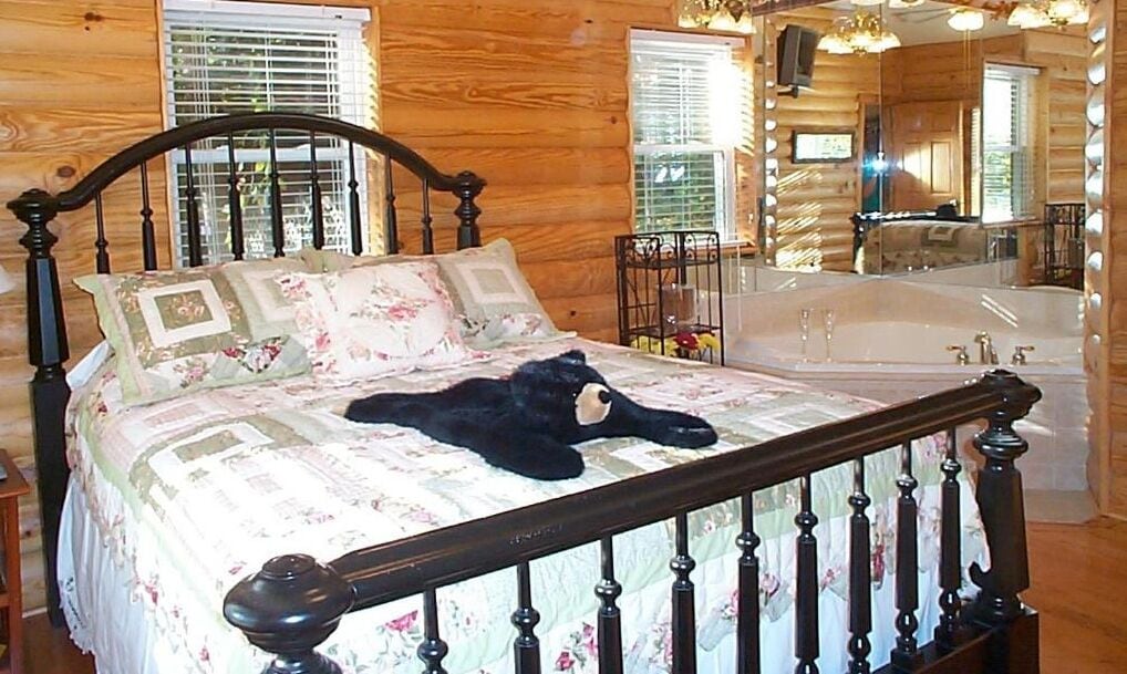 Een slaapkamer in een houten chalet, met een bed, een grote spiegel en een bad.