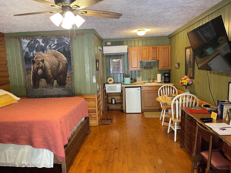 A cozy room with a bed, a desk, a chair, a small kitchenette, and a ceiling fan.