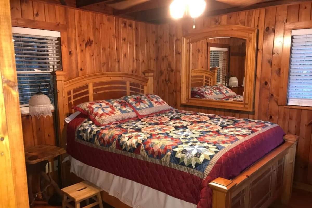 A wooden-paneled bedroom with a large bed, a mirror, and a small stool.