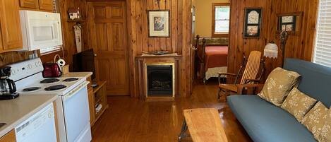 A cozy cabin-style room with wooden walls, a fireplace, a dining area, and a living room with a sofa and bench.