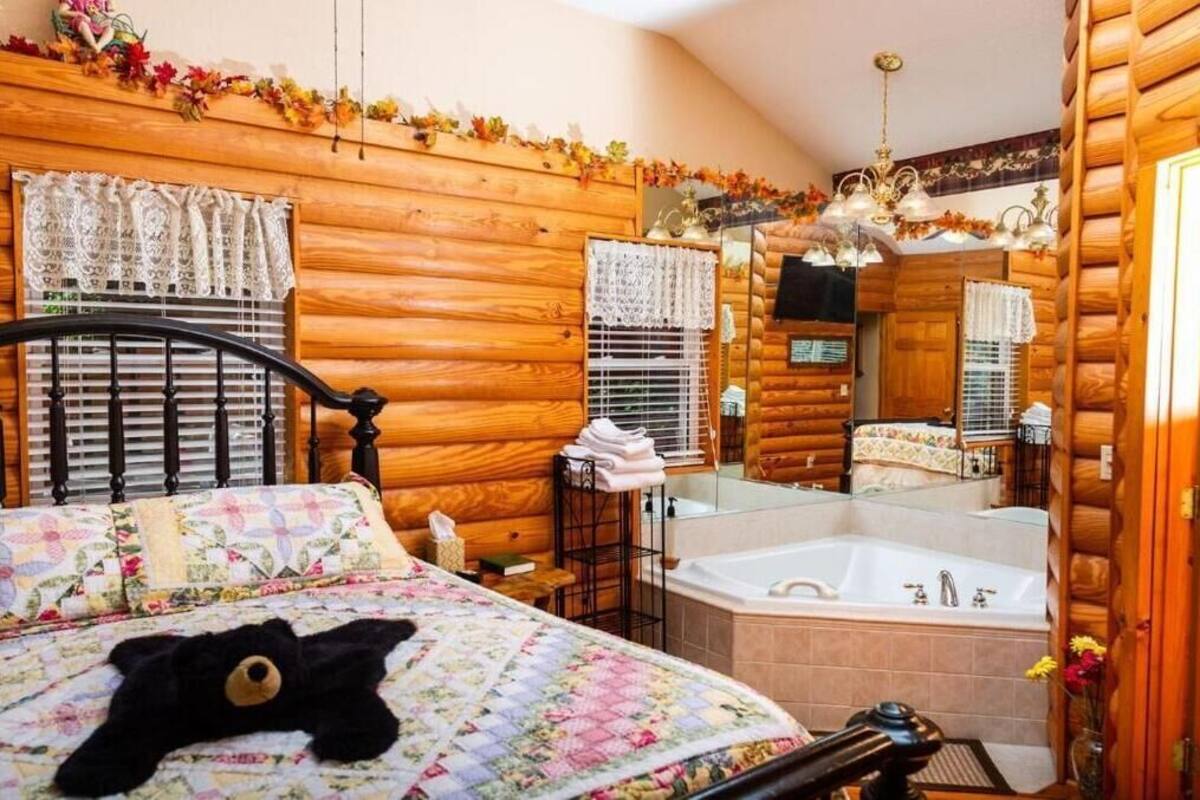 A cozy log cabin bedroom with a bed, a large mirror, a window with lace curtains, and a wooden ceiling.