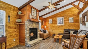 A log cabin interior with a stone fireplace, wooden furniture, and wooden walls. - 3 King Bedrooms with Hot Tub Game Room Fire Pit Pool Table Putting Room (Townsend)