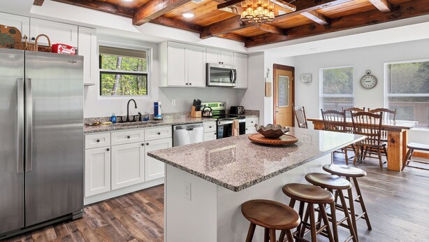 A modern kitchen with white cabinets, a stainless steel refrigerator, a granite countertop, and a wooden ceiling. - 3 King Bedrooms with Hot Tub Game Room Fire Pit Pool Table Putting Room (Townsend)