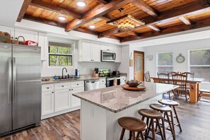 A modern kitchen with white cabinets, a stainless steel refrigerator, a granite countertop, and a wooden ceiling. - 3 King Bedrooms with Hot Tub Game Room Fire Pit Pool Table Putting Room (Townsend)