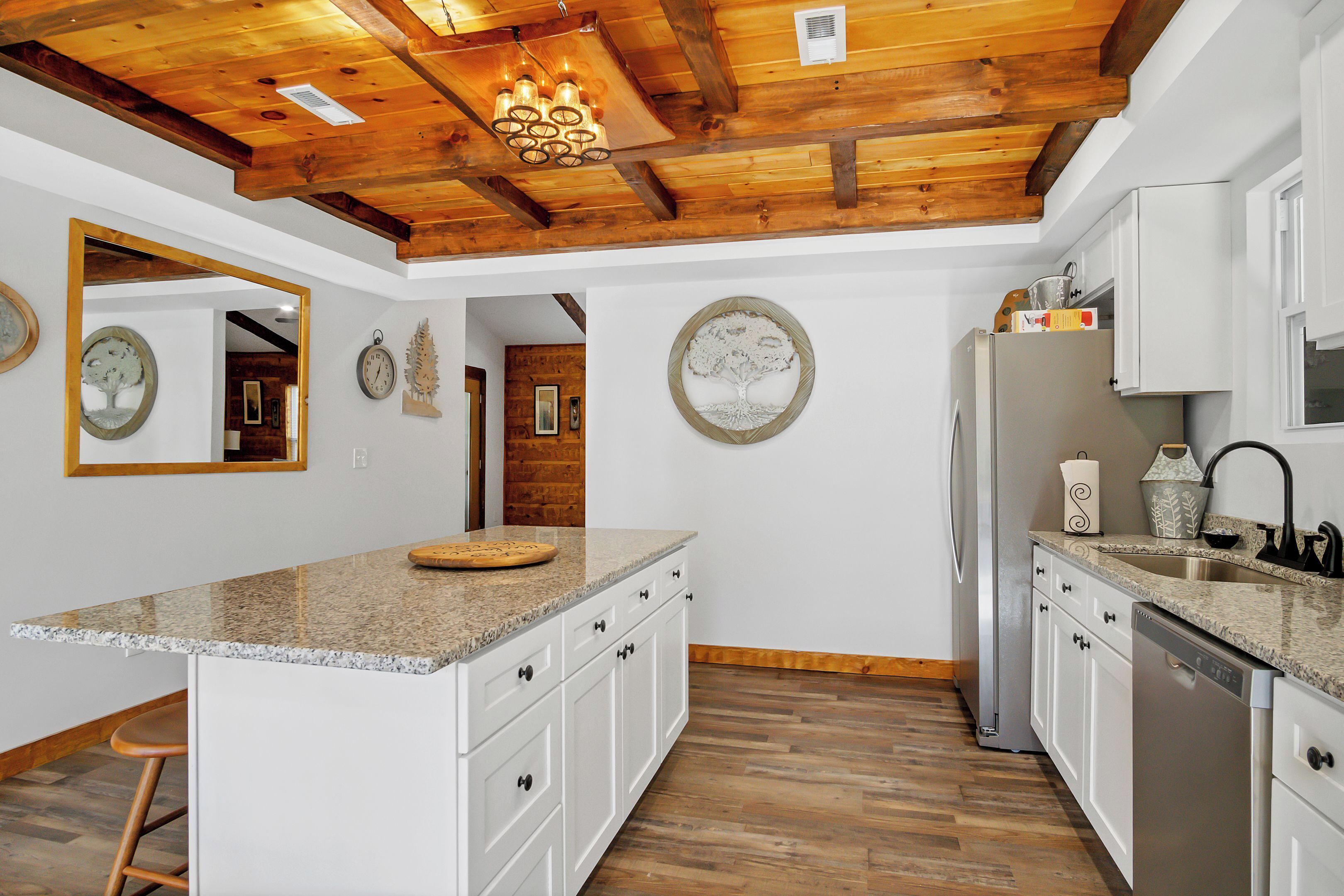A kitchen with wooden beams, granite countertops, white cabinets, and a stainless steel refrigerator.