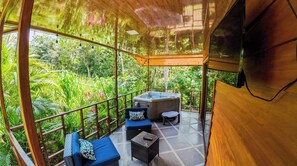 A modern outdoor lounge area with a hot tub, seating, and a view of lush greenery.
