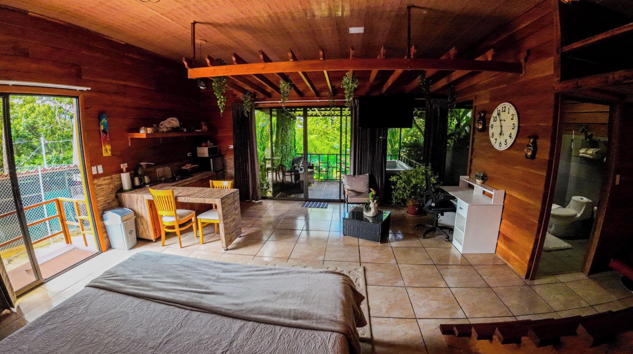 A wooden cabin with a bed, a dining area, a kitchen, and a bathroom.