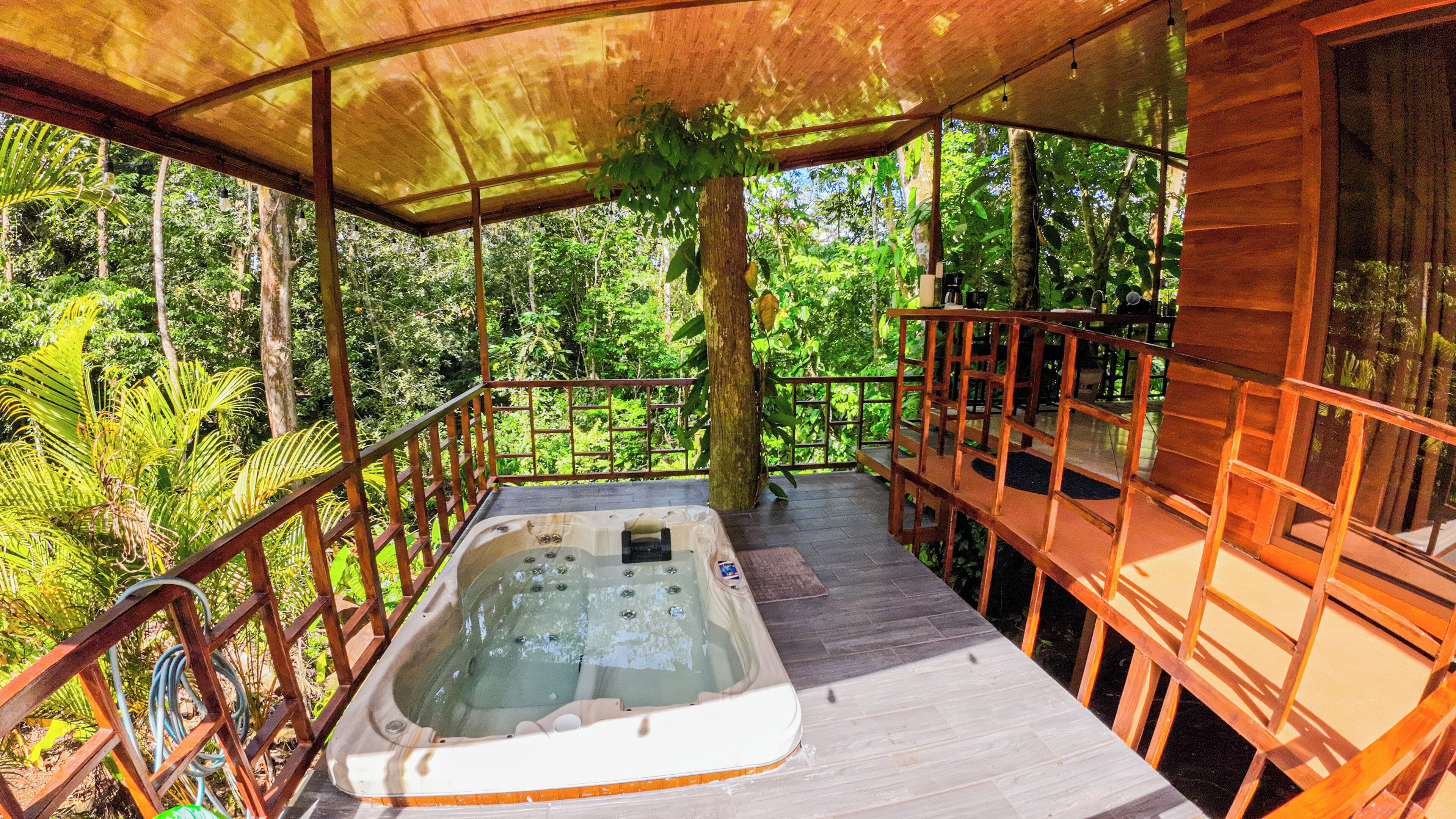 A wooden deck with a hot tub, surrounded by a wooden railing and a canopy.