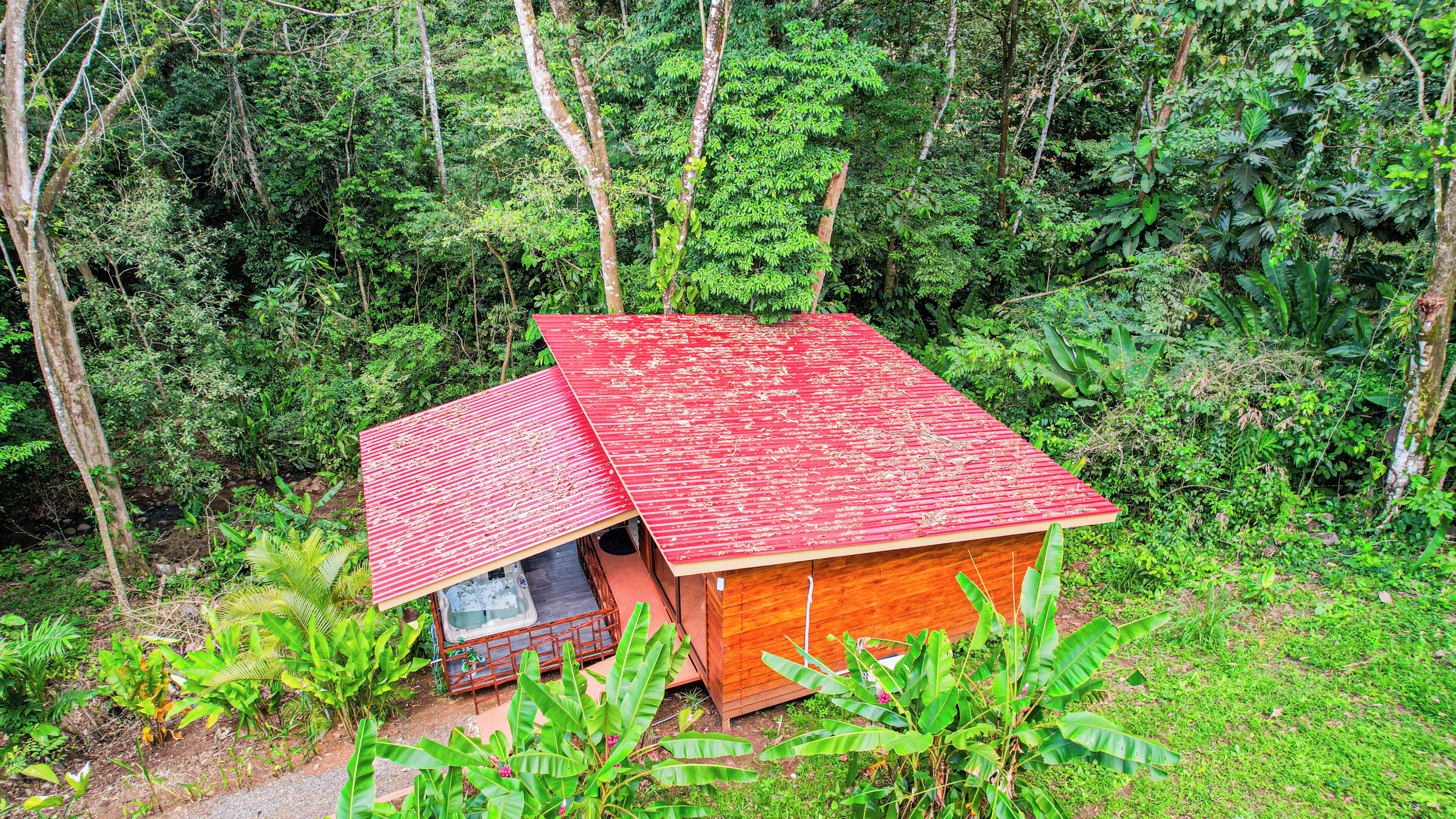 Una pequeña cabaña de madera con techo rojo, rodeada de un denso bosque.