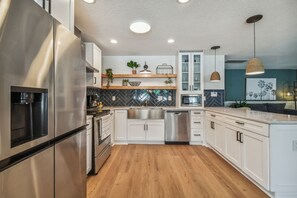 Una cocina moderna con electrodomésticos de acero inoxidable, suelo de madera y armarios blancos.