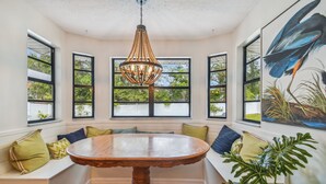 Un espace repas avec une table en bois et des bancs, de grandes fenêtres à cadres noirs et un luminaire suspendu.