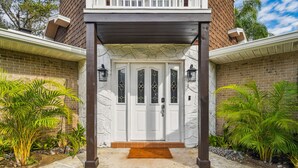 Une maison avec une porte d’entrée blanche, un porche couvert et une façade en briques.