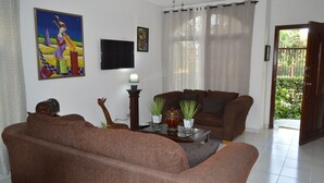 Una sala de estar con dos sofás marrones, una mesa de centro con adornos, un televisor en la pared y una puerta que da a un jardín.