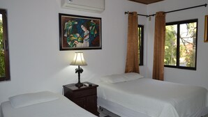 Habitación de hotel con dos camas, una mesita de noche con lámpara, un cuadro en la pared y una ventana con cortinas.