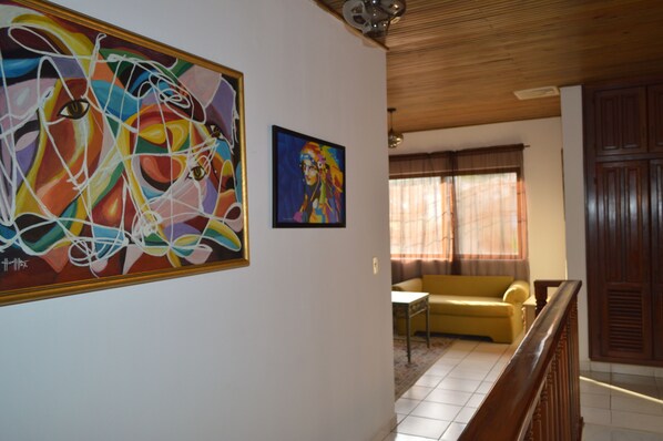 Una habitación con un cuadro abstracto grande en la pared, un cuadro más pequeño, un sofá amarillo y una escalera de madera.