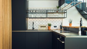 A modern kitchen with black cabinets, a herringbone wood floor, a built-in oven, and a black staircase with glass railings.