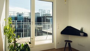 A room with a sliding glass door leading to a balcony, a small stool, and a wall-mounted shelf with a plant.