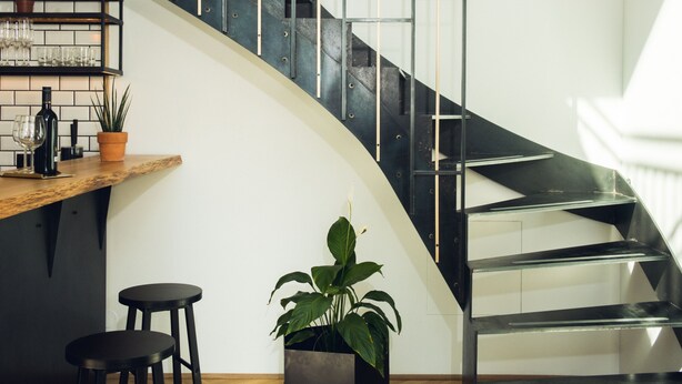 A modern interior with a curved staircase, a bar area with stools, and potted plants.