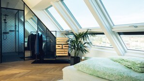 A bedroom with a skylight, wooden flooring, a bed with green patterned bedding, a potted plant, and a clothing rack.