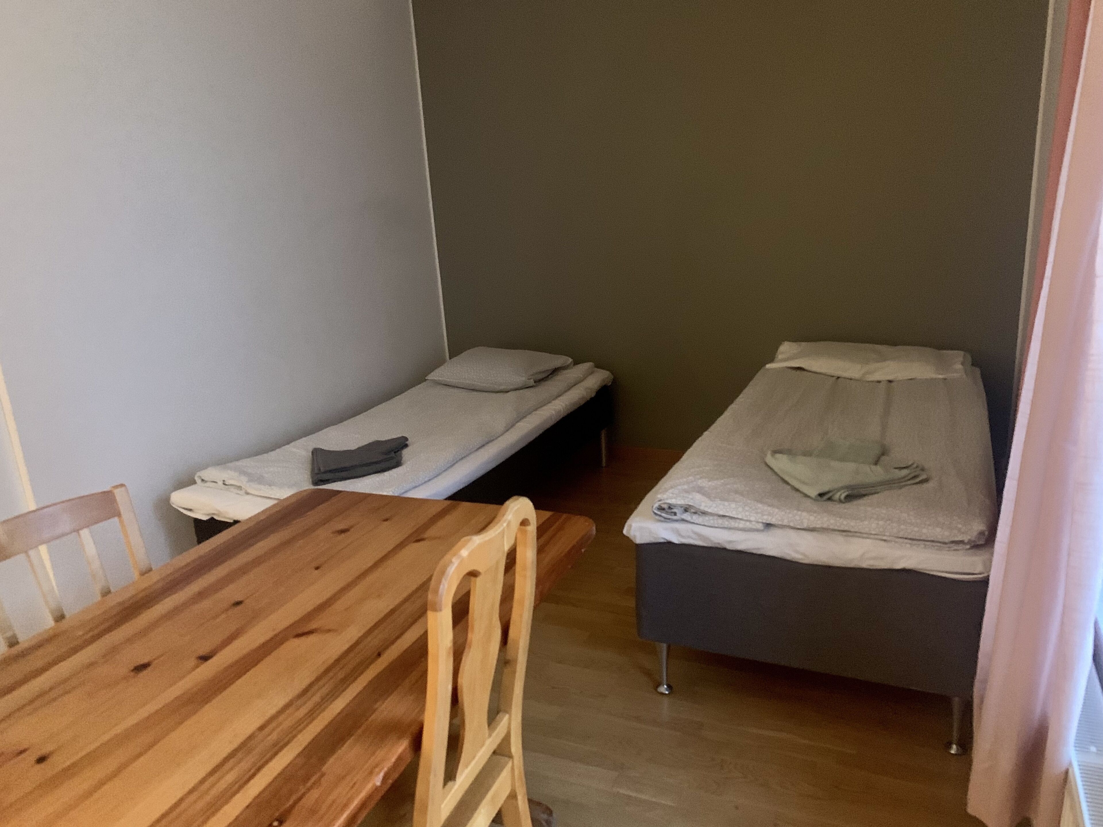 Een kleine kamer met twee eenpersoonsbedden, een houten tafel en een stoel.
