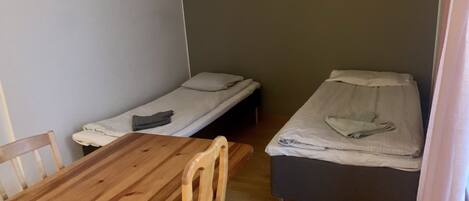 Een kleine kamer met twee eenpersoonsbedden, een houten tafel en een stoel.
