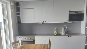 A modern kitchen with white cabinets, a wooden dining table, and a built-in oven. - Apartment in Sundbyberg , Stockholm (Sundbyberg)