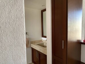 A bathroom with a beige countertop sink, a mirror, and wooden cabinets. - Mission Suites Juriquilla (Querétaro)