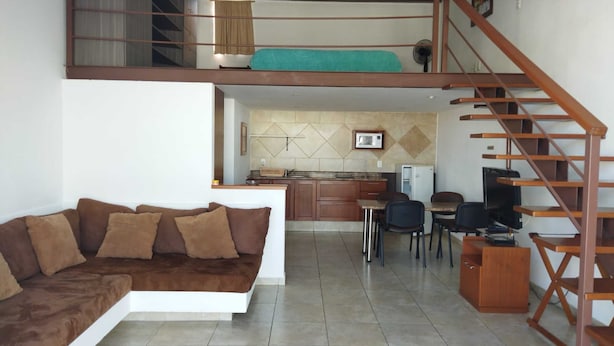 Espaço tipo loft com sofá, área de refeições, cozinha e escada.